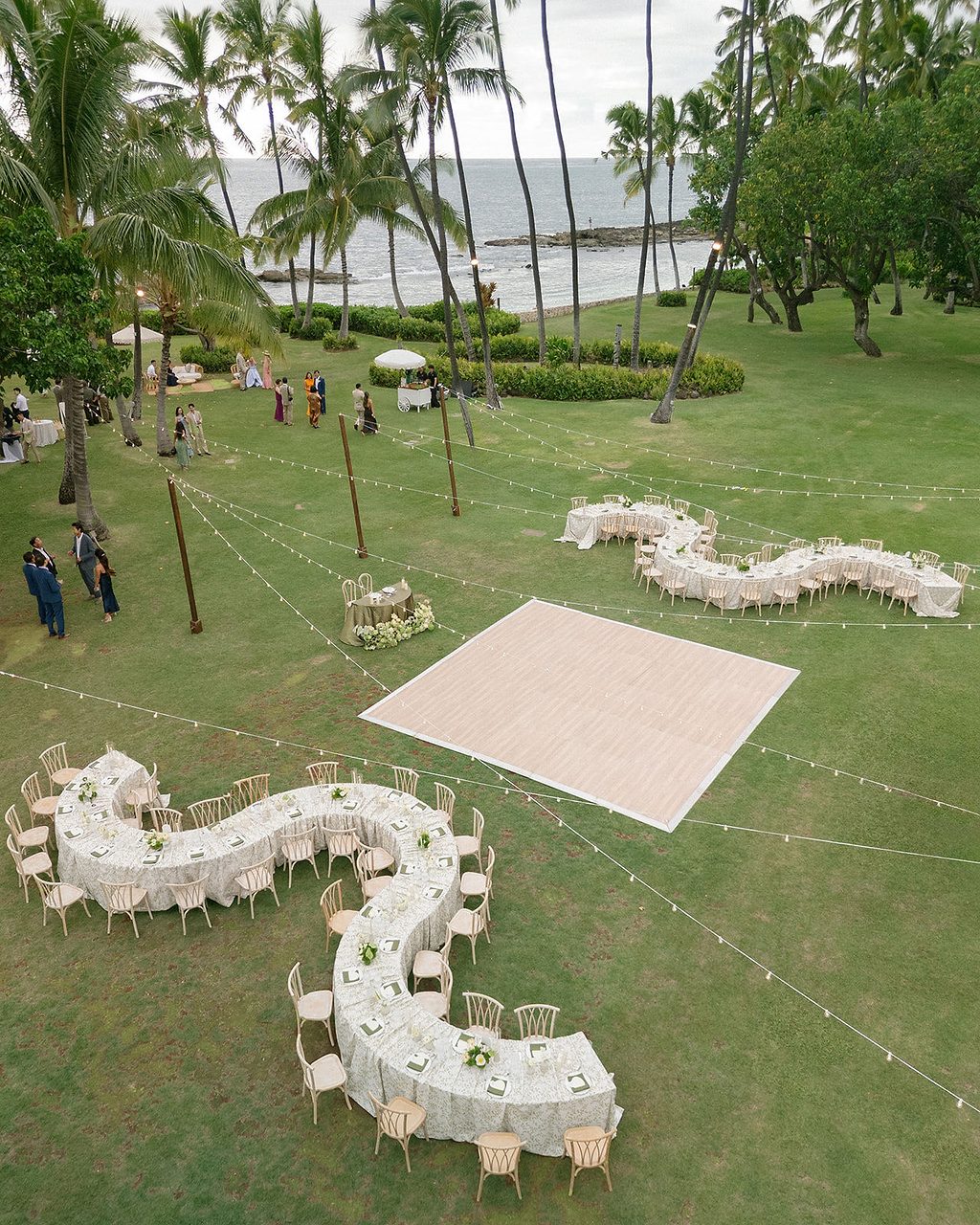 Aerial view of curved reception tables on an oceanfront lawn on Oahu