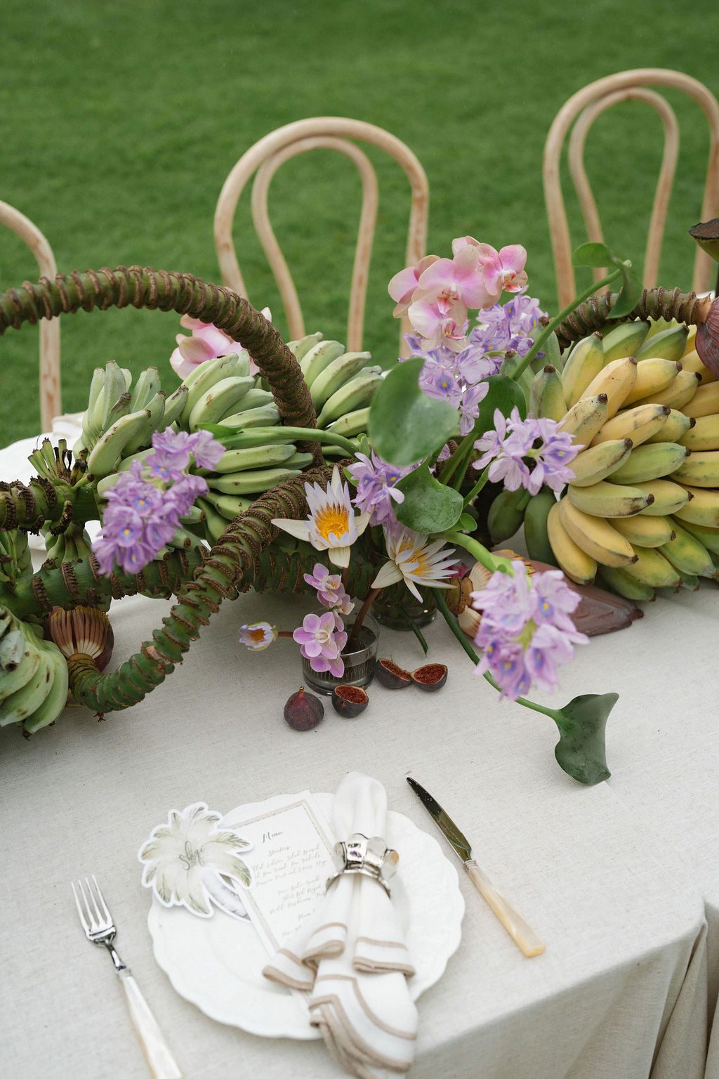 Banana stalk and orchid centerpiece with water lilies above a scalloped plate setting