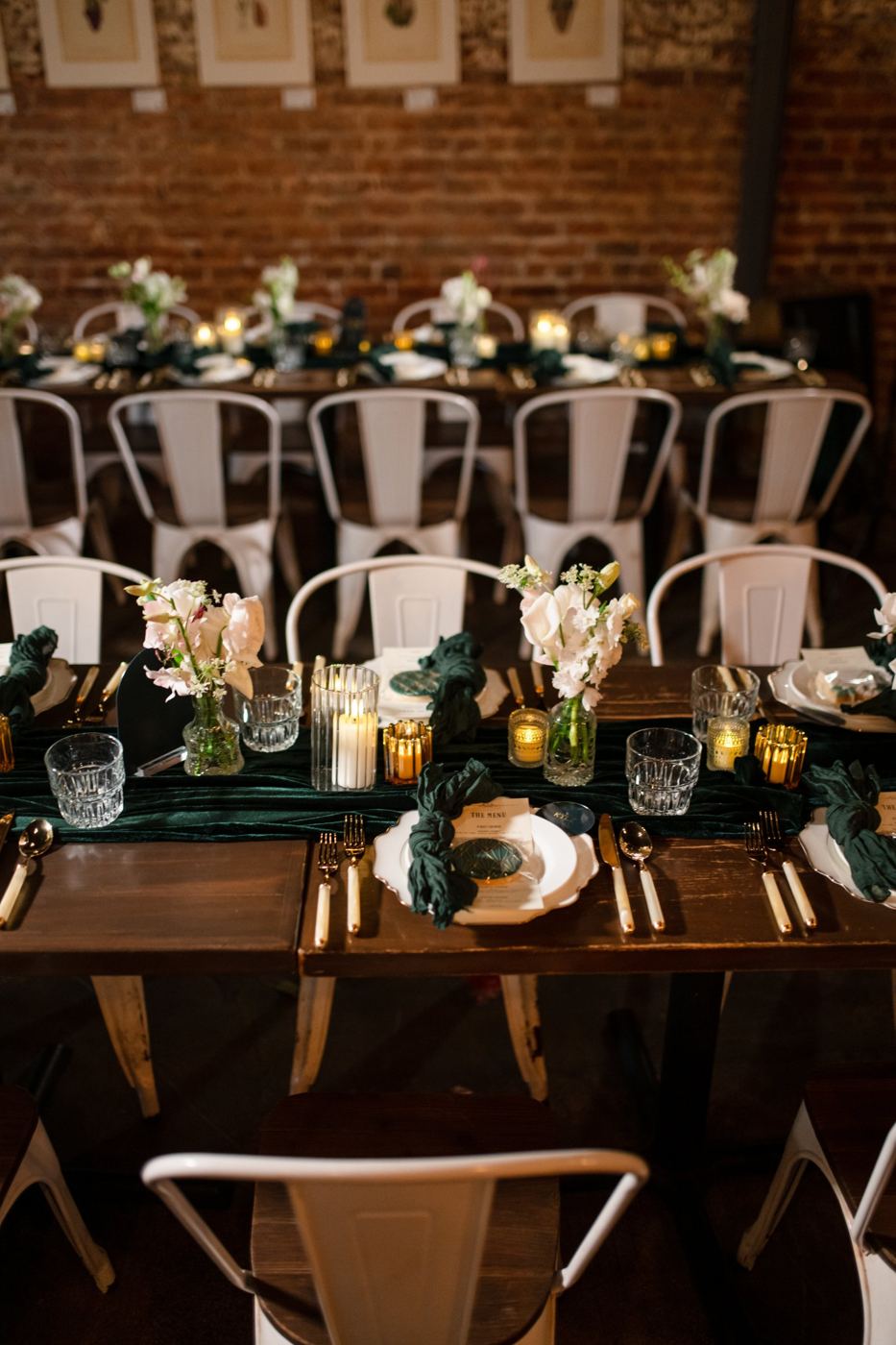 Long dinner tables with candlelight and white florals against a brick wall