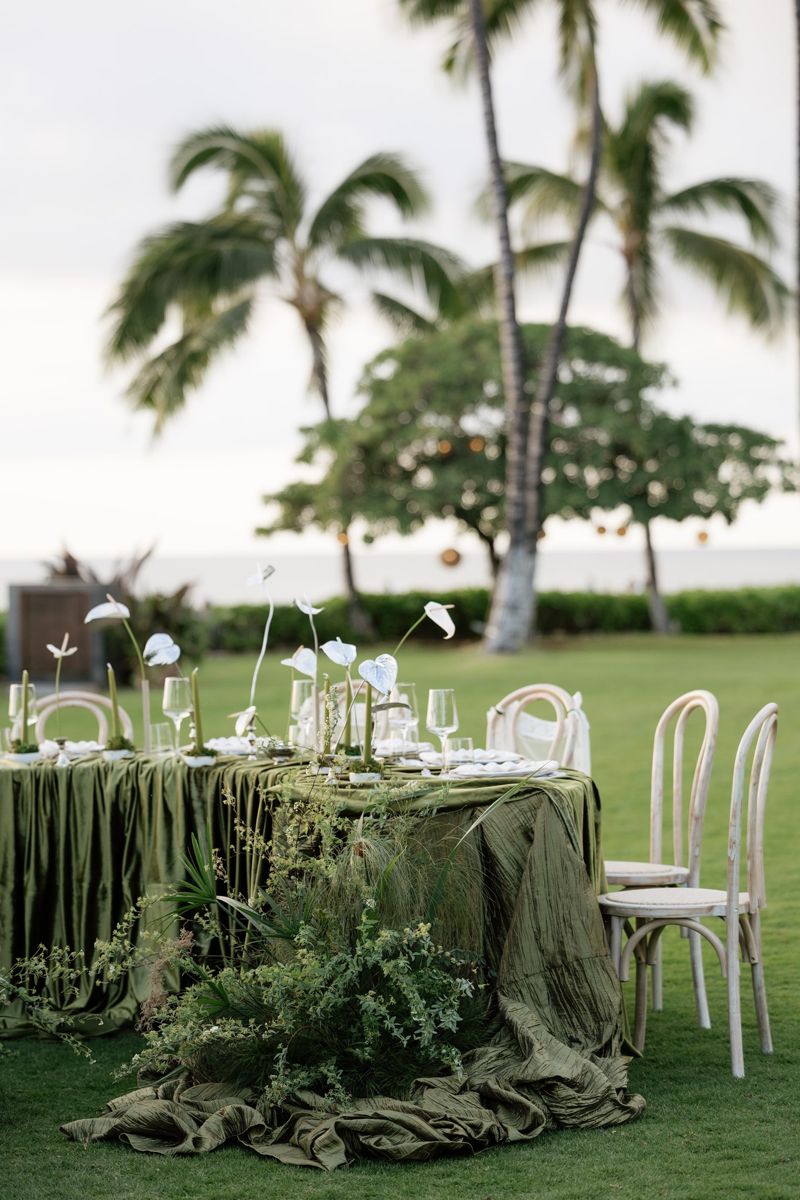 Olive velvet table with white anthuriums and green tapers under coconut palms by the ocean