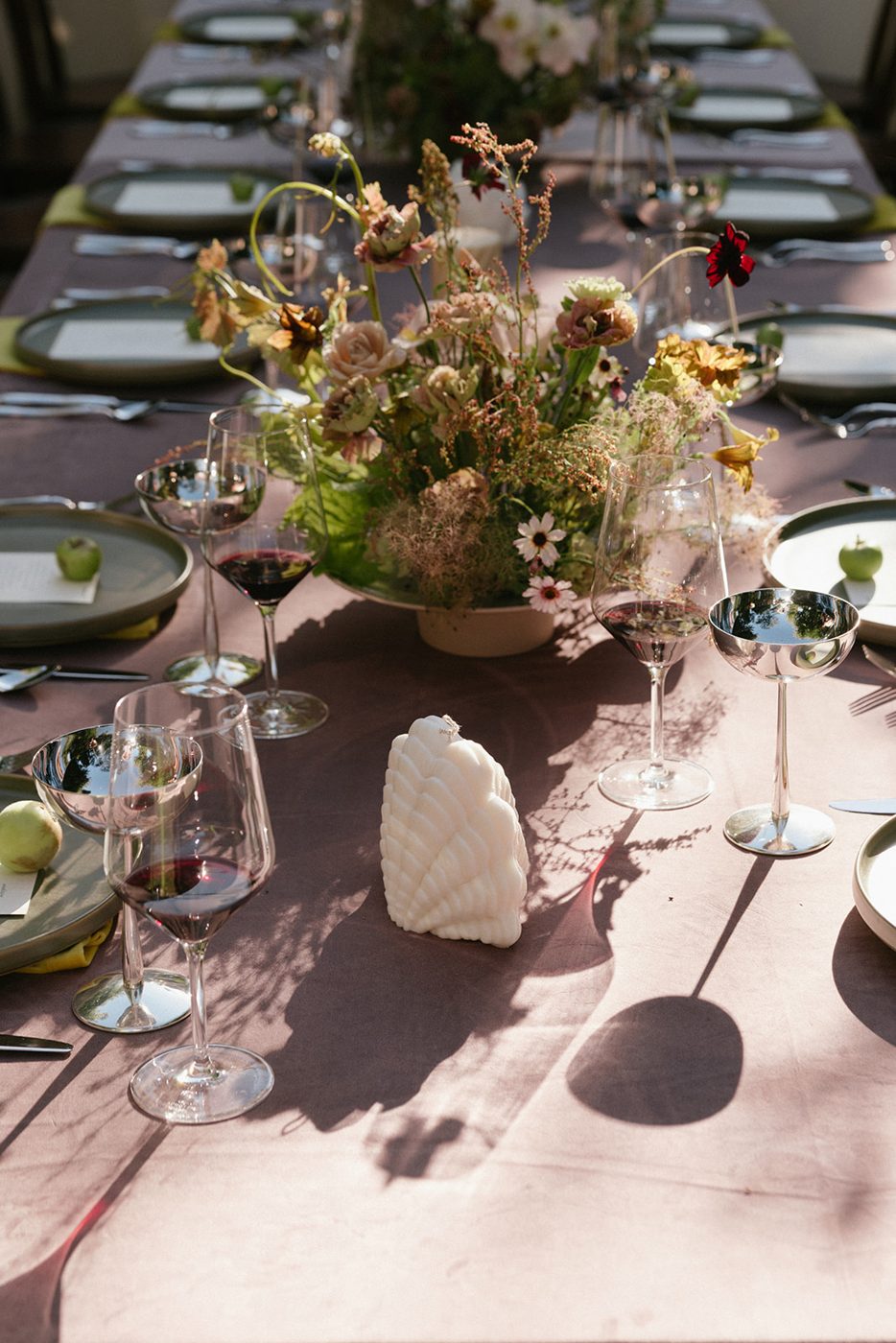 Wild floral centerpiece with Lustra stainless coupes, wine glasses and a shell candle on a garden table