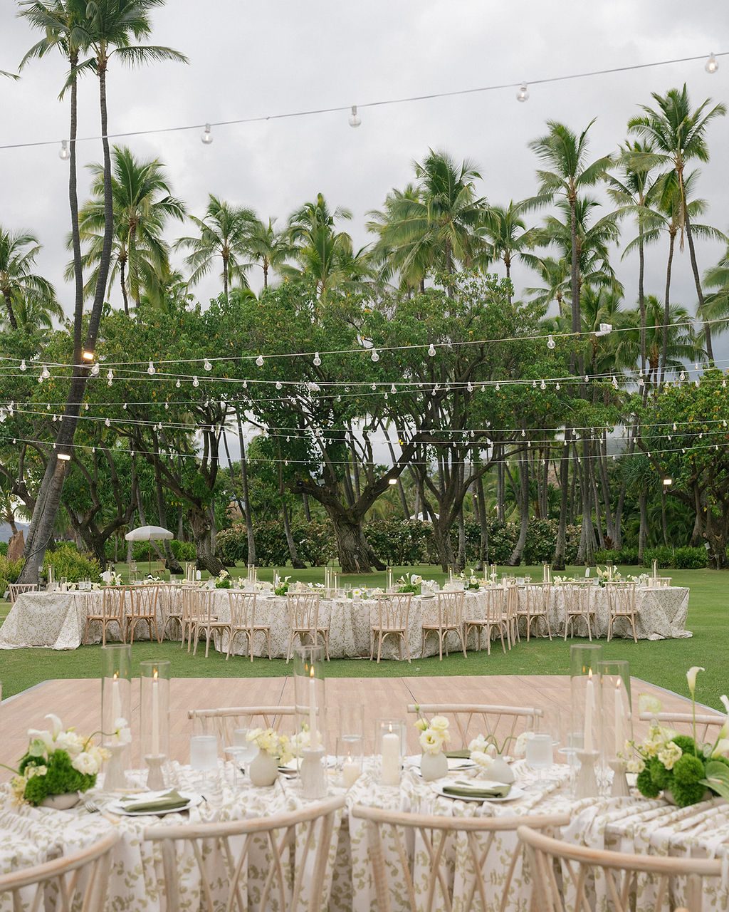 Wedding tables under string lights and tall palms on Oahu