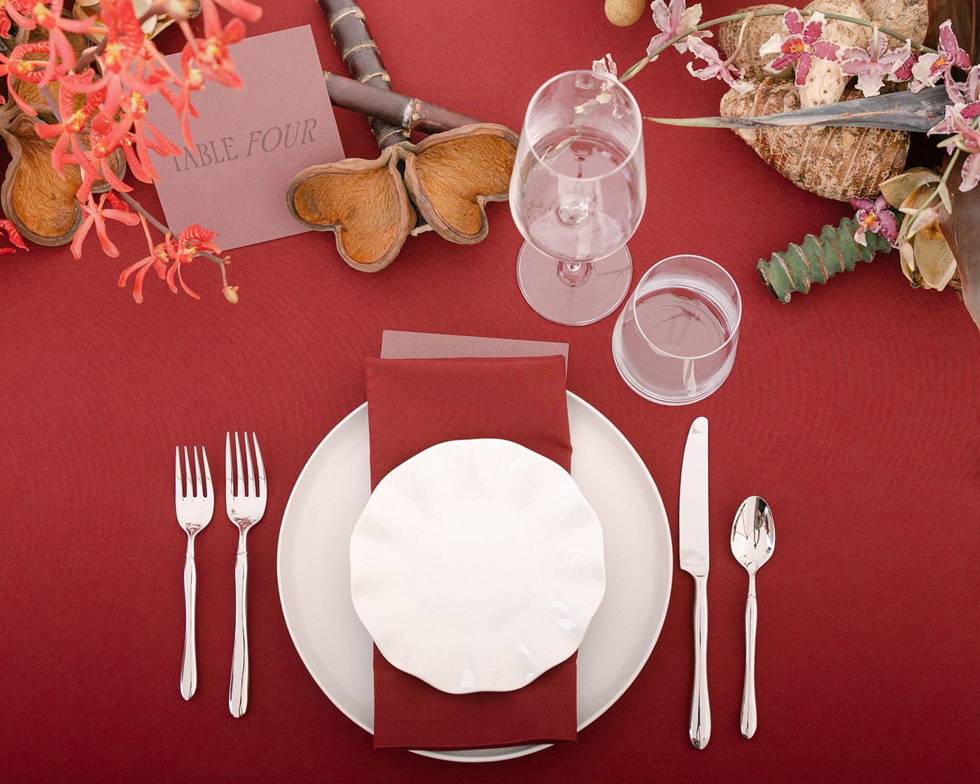 Overhead view of a place setting: two forks, dinner plate, wavy salad plate, knife and spoon, wine and water glasses, and a Table Four card